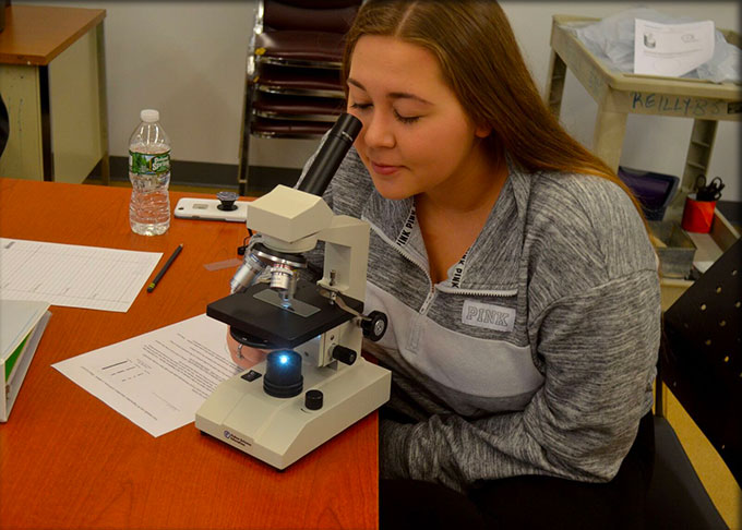 Student sitiing at a microscope in a science class